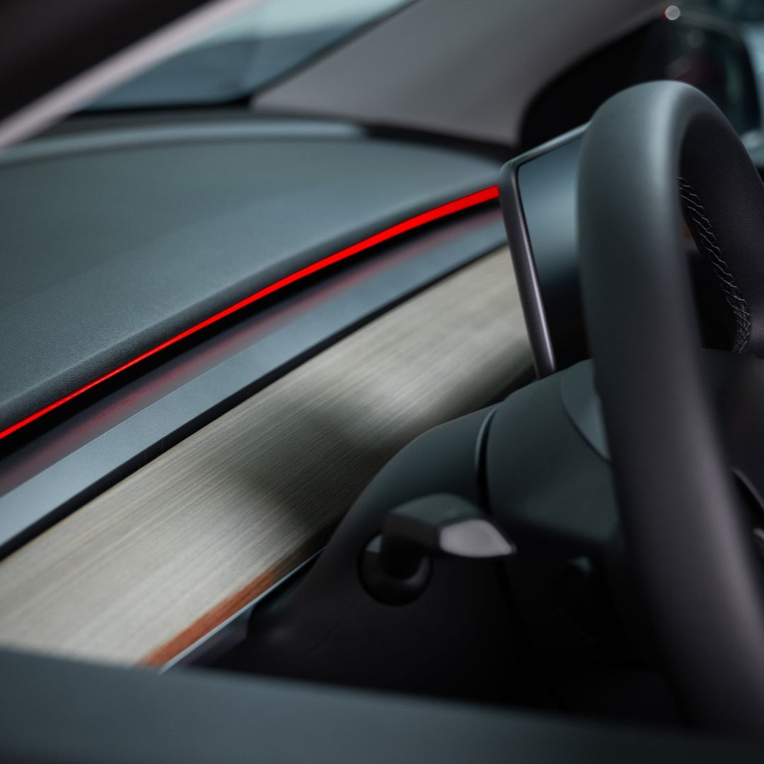 Close-up of red S3XY Strip ambient lighting above the dashboard trim beside a Tesla steering wheel.