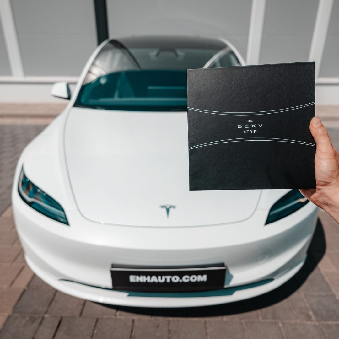 Hand holding a black S3XY Strip product box in front of a white Tesla.